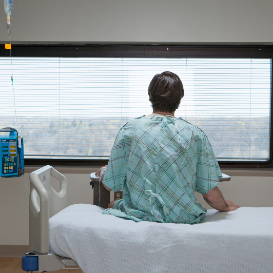 Paciente sentado sobre la cama de un hospital,, mirando hacia la ventana de la habitación