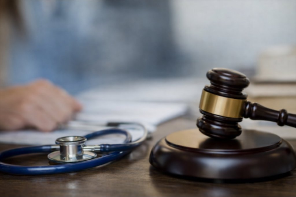 Escritorio con estetoscopio y martillo del juez, esfumado se ve la imagen de una mano sobre papeles